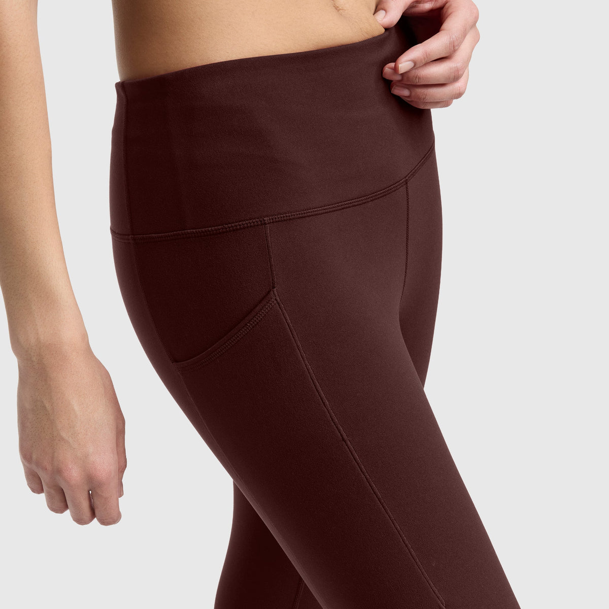 A person wearing high-waisted, dark brown Champion Leggings, C Logo with pockets, shown from mid-torso to thigh against a plain light background.