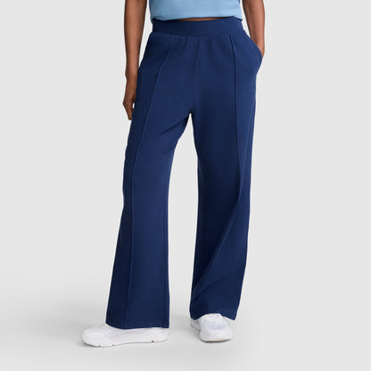 A person wearing Champion Open Bottom Pant in navy blue stretch jersey, paired with a light blue top and white sneakers, stands against a light grey background.
