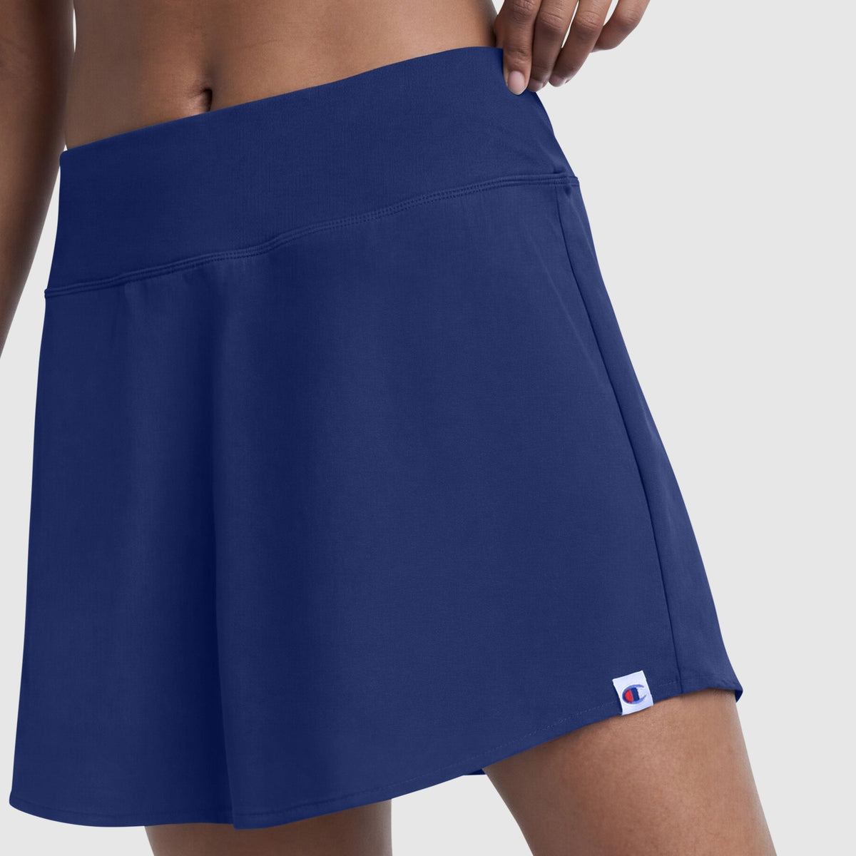 A person models the Champion Courtside Skort, featuring a small C logo near the hem, in navy blue on a plain light background, highlighting classic court style.