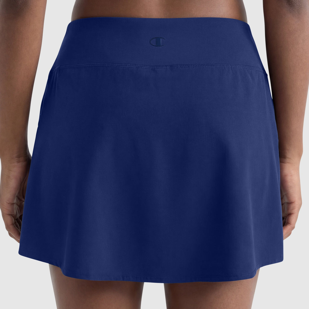 Rear view of a person wearing the Champion Courtside Skort with C Logo in navy blue, featuring a wide, smooth waistband and small logo at the center back for a polished athletic look. Hands are relaxed at their sides.