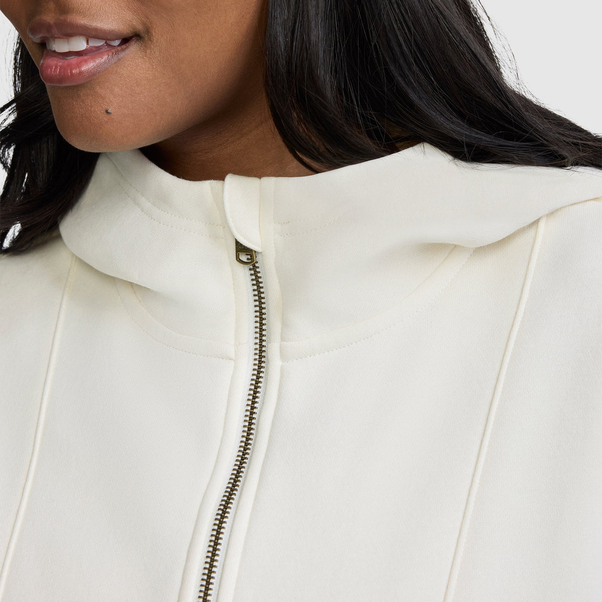 A close-up of a woman wearing a cozy off-white Champion Training Half-Zip Fleece Hoodie, smiling slightly. Only her lower face, neck, and chest are visible in this athletic pullover.