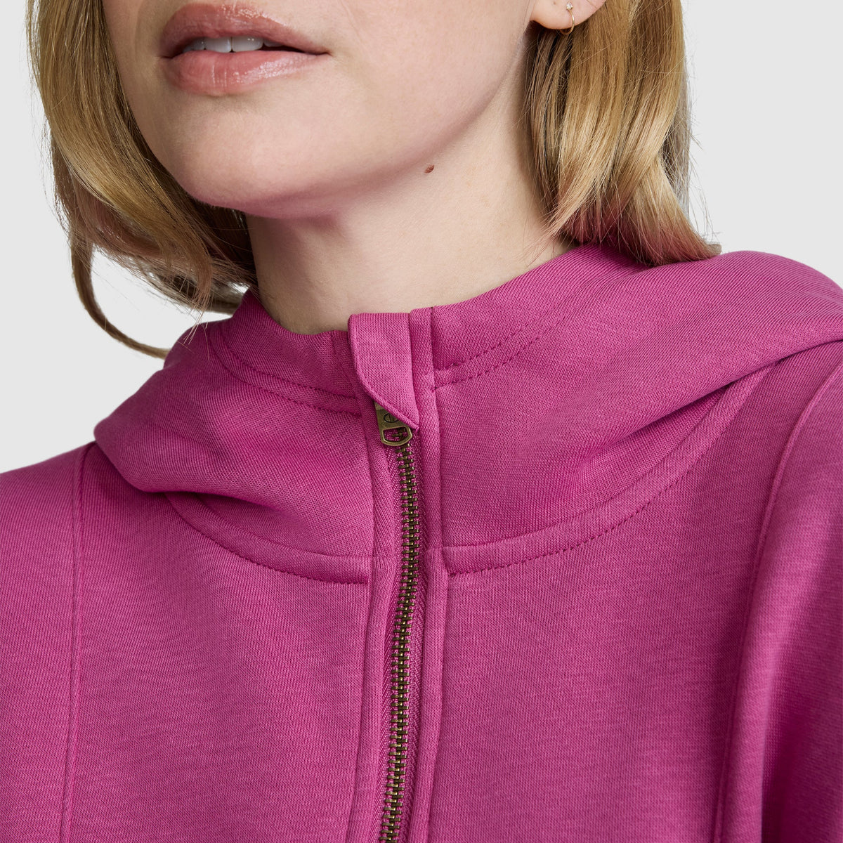 A close-up of a woman wearing a bright pink Champion Training Half-Zip Fleece Hoodie. The image highlights the lower part of her face and upper chest, focusing on the hoodie’s zipper and neckline.