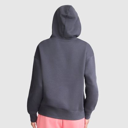 A person is seen from the back against a plain light gray background, wearing a Champion Fleece Hoodie with satin applique in dark gray, hood up, paired with light pink pants.