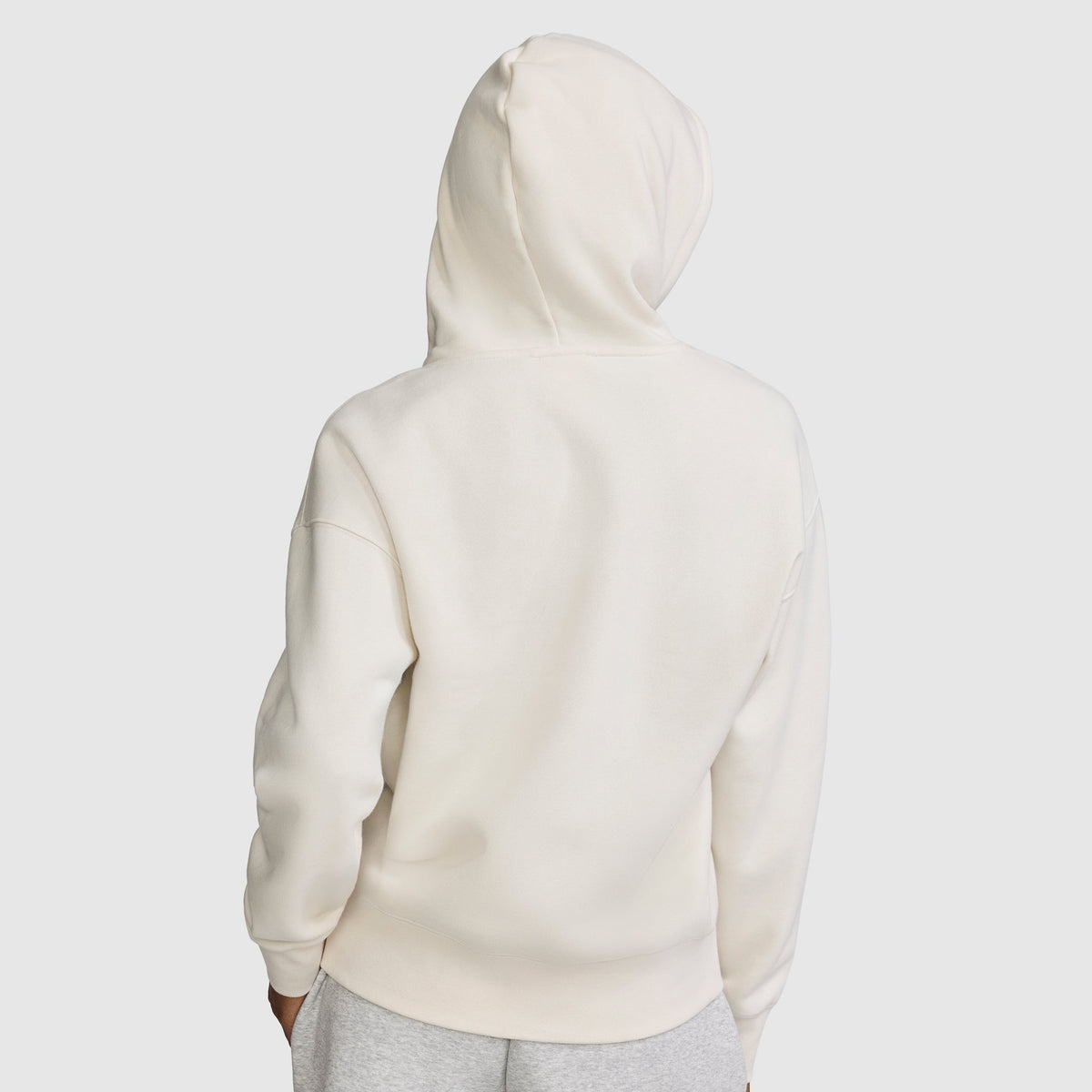 A person wearing a plain white Champion Fleece Hoodie, Satin Applique, with the hood up is viewed from the back. They are also wearing light gray pants against a light gray background.