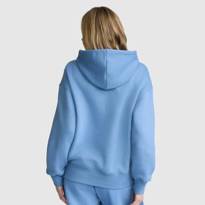 A person with blonde hair is seen from behind, wearing the Champion Fleece Hoodie with satin applique and matching sweatpants, standing against a plain white background.
