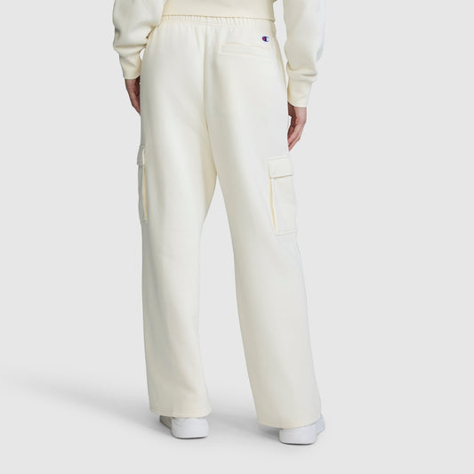 A person is seen from the back, standing against a plain white background, wearing the Champion Fleece Cargo Training Pant in a cream color paired with a matching sweatshirt. The pants feature side and back pockets, delivering comfort and utility for everyday wear.