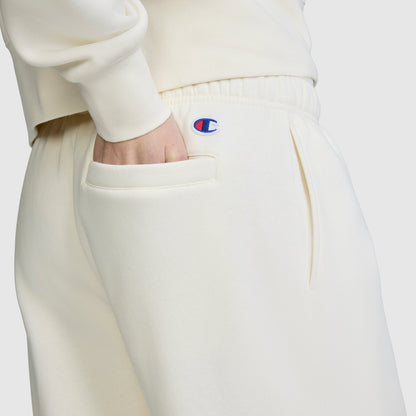 A person wearing the Champion Fleece Cargo Training Pant in cream, with a hand in the side pocket, displays the blue and red Champion logo near the waistband against a plain background.