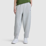 A person is shown from the waist down, wearing the Champion Barrel Leg Fleece Pant in light gray, paired with a green shirt and white sneakers, against a plain white background. The relaxed fit of these Champion women’s pants is prominently displayed.