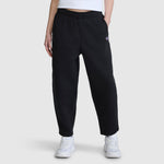 A person is wearing the Champion Barrel Leg Fleece Pant, crafted from midweight cotton-poly fleece in black, paired with a white cropped top and white sneakers, standing against a plain light gray background.