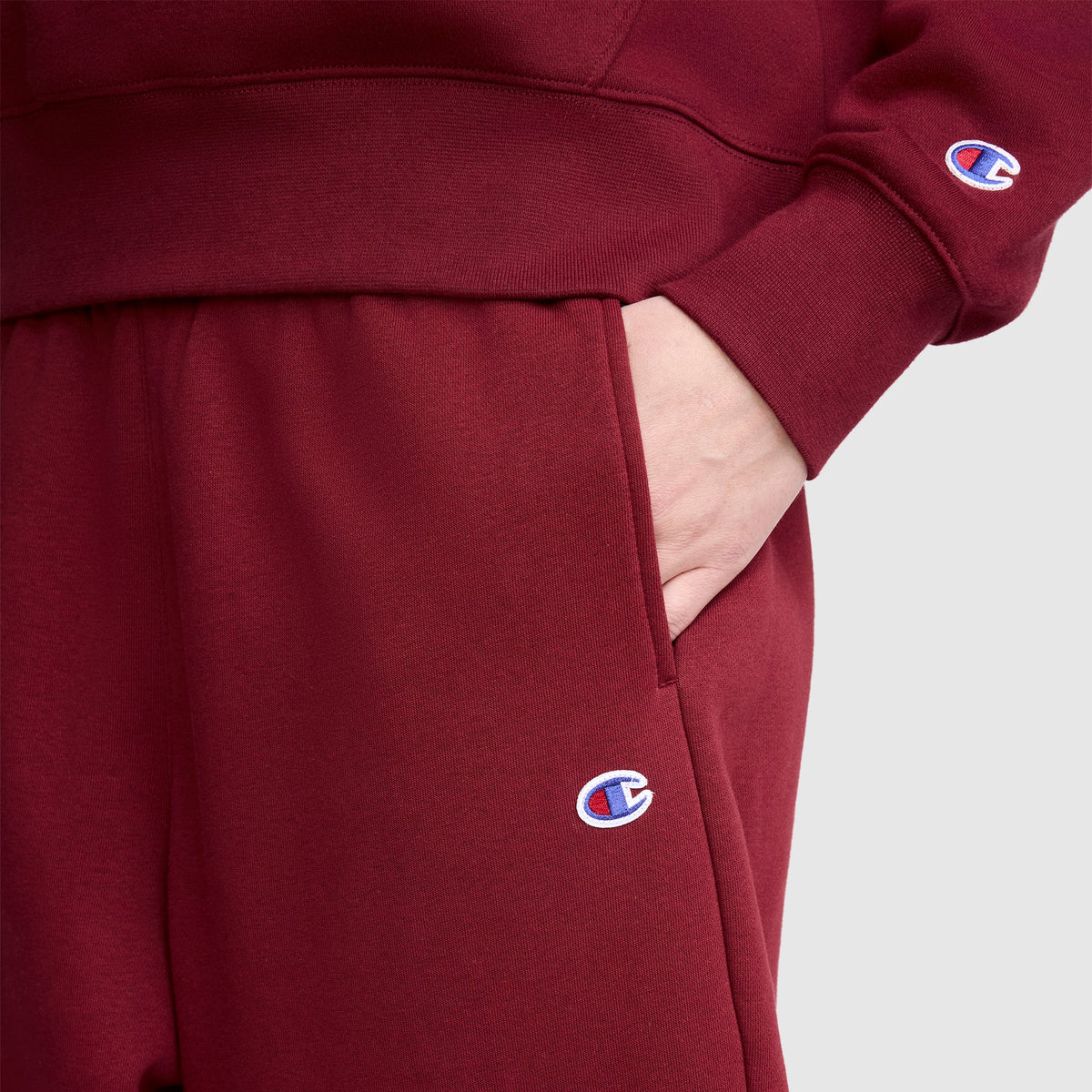 A person wearing matching maroon Champion sweatshirt and Barrel Leg Fleece Pant, with a hand in the pocket. Both garments display the Champion logo, and the pants are styled for a trendy, relaxed fit.