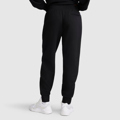 A person is seen from the back, standing against a plain light gray background, wearing the Champion Taper Leg Jogger with Zippers in black paired with white sneakers.