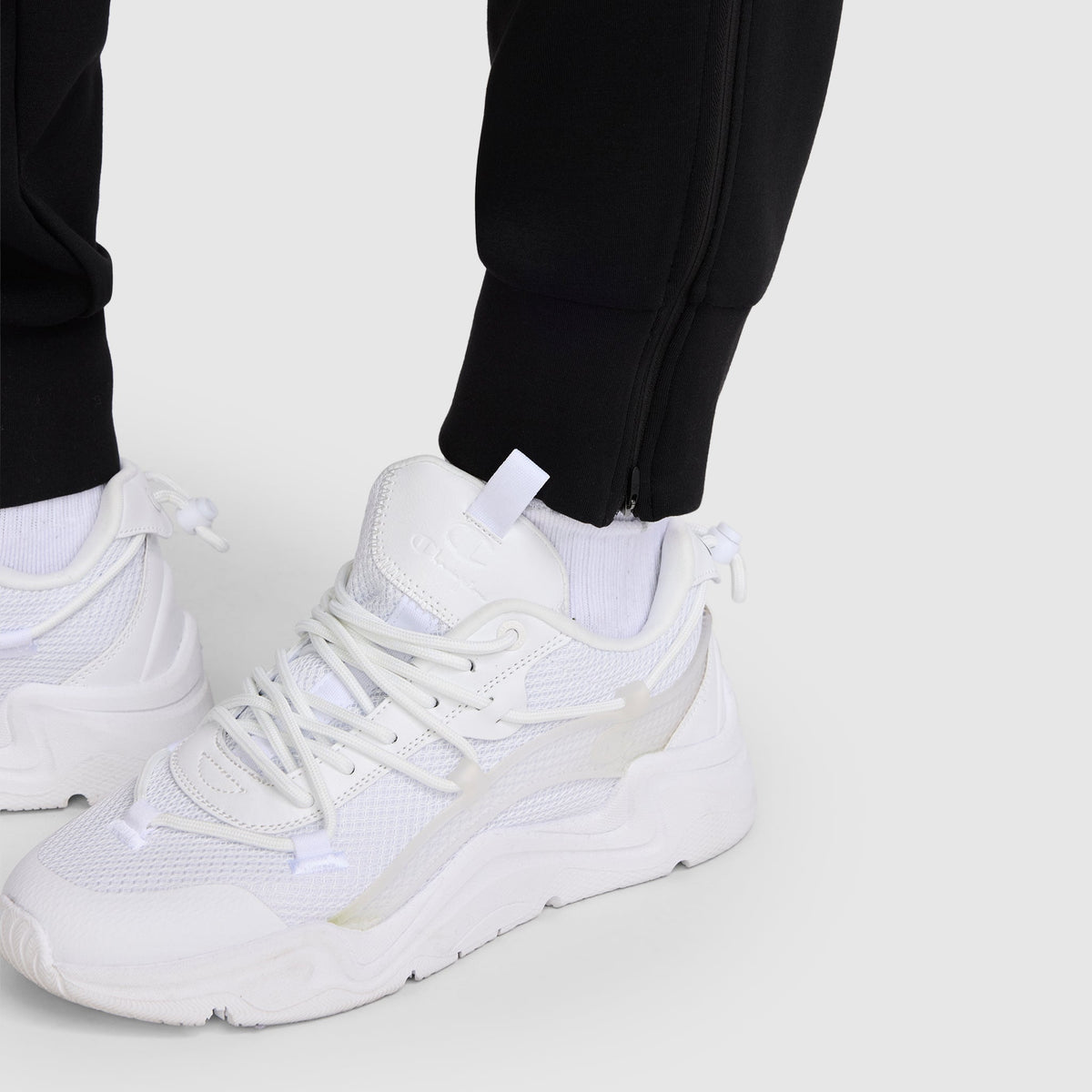 A person wearing white sneakers and the Champion Taper Leg Jogger with Zippers stands on a light gray surface.