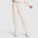 A person is shown from the waist down, wearing Champion Taper Leg Jogger with Zippers in light beige paired with a matching sweatshirt and white athletic shoes, standing against a plain light background. The joggers feature a modern tapered leg design.