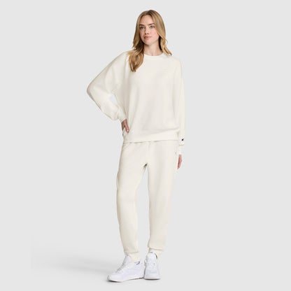 A woman stands against a plain light gray background, wearing an all-white modal scuba blend sweatshirt and Champion Taper Leg Jogger with Zippers, paired with white sneakers.