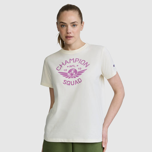 A woman stands against a plain background with one hand in her pocket, wearing the Champion Squad Graphic T-Shirt—a white tee featuring a collegiate-inspired purple winged basketball graphic. Made from lightweight cotton jersey, this shirt delivers all-day comfort and effortless style.
