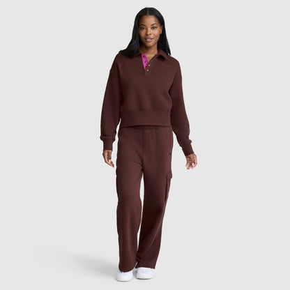 A woman stands against a plain light gray background, wearing the Champion Fleece Training Polo paired with matching pants and white sneakers.