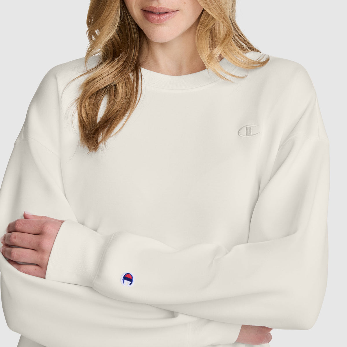 Off-white long-sleeve modal scuba Crewneck Pullover Sweatshirt by Champion, featuring a small embroidered logo on the chest and a patch logo on the left cuff.