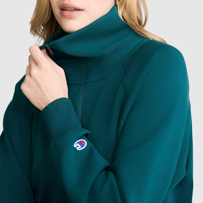 A person wearing a teal Champion Quarter-Zip Pullover with a high collar, partially zipped up. The athletic pullover has a small Champion logo patch near the wrist.