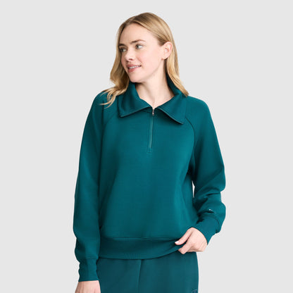 Wearing the Champion Quarter-Zip Pullover in teal stretch poly-modal, paired with matching pants, a person stands against a plain light gray background, looking to the side and smiling softly.