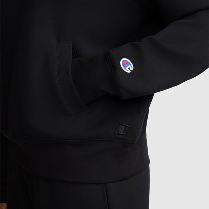 A person is wearing a Champion Quarter-Zip Pullover in black, with one hand tucked into the front pocket and the Champion logo patch visible on the sleeve. The photo is cropped to show the athletic pullover from shoulder to upper thigh.