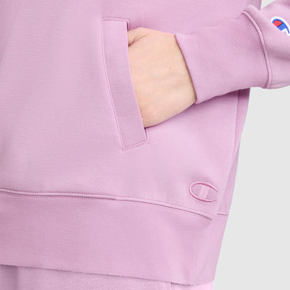 A person wearing a light purple Champion Quarter-Zip Pullover with one hand in the front pocket. The fabric features a small embroidered Champion logo near the wrist and another near the hem, showcasing the sporty design of this women's athletic Quarter-Zip Pullover.