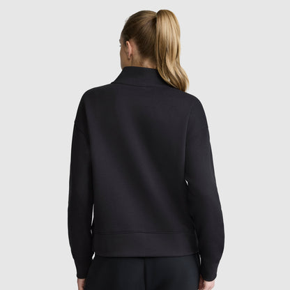 A woman with blonde hair in a ponytail is shown from behind, wearing a black Champion Fleece Mockneck Quarter-Zip and matching black pants against a plain light gray background, embodying effortless sport style.