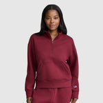A woman wearing a Champion Fleece Mockneck Quarter-Zip sweatshirt and matching pants in maroon stands facing forward with her hands in the front pocket, embodying sporty style against a light gray background.