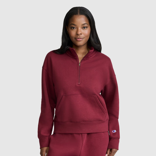 A woman wearing a Champion Fleece Mockneck Quarter-Zip sweatshirt and matching pants in maroon stands facing forward with her hands in the front pocket, embodying sporty style against a light gray background.