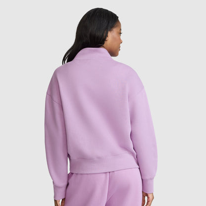 A woman with long dark hair is shown from the back wearing a light purple Champion Fleece Mockneck Quarter-Zip sweatshirt and matching sweatpants in a sport style, set against a plain light gray background.