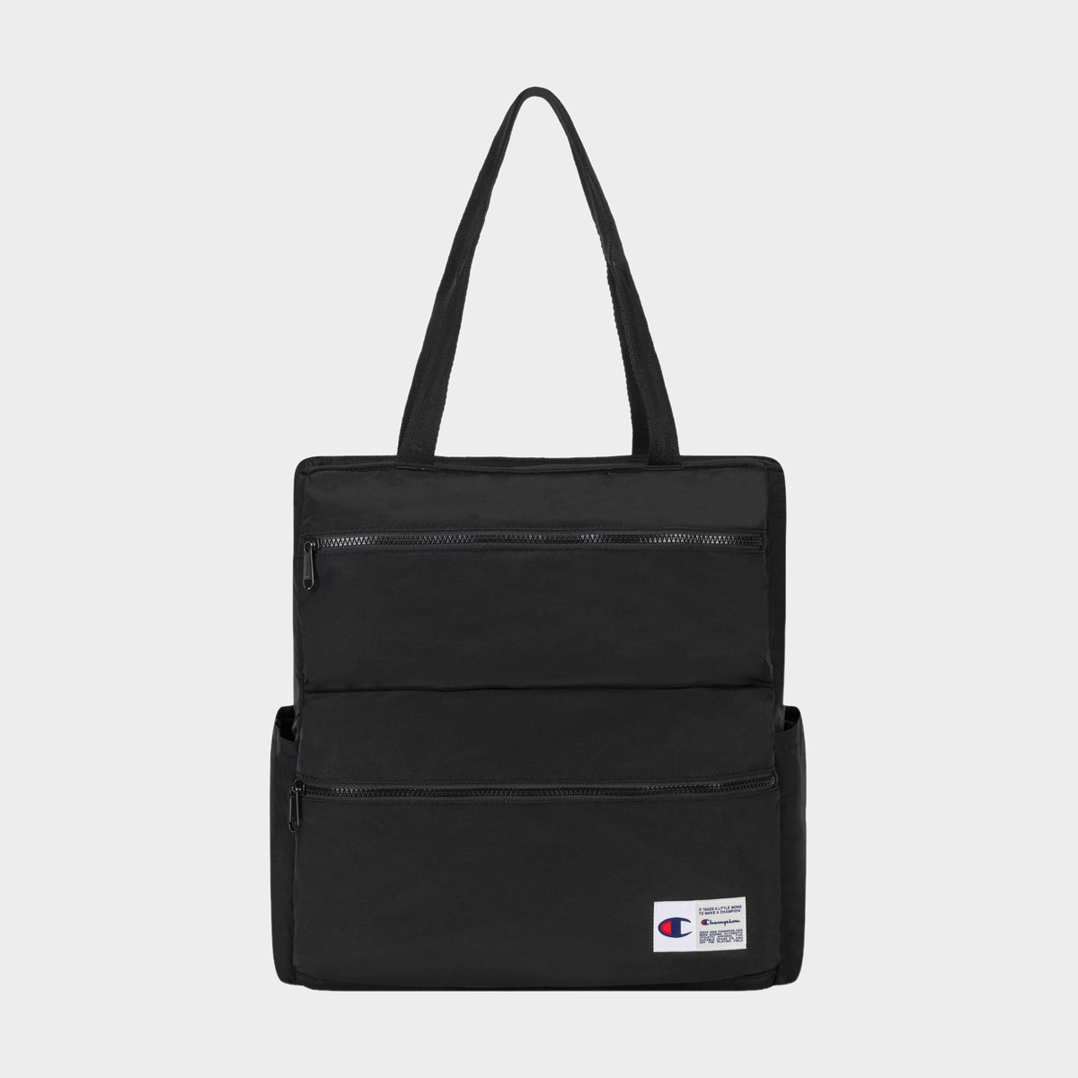 The Champion Explore Tote is crafted from durable crinkle nylon in black and features two zippered front pockets, convenient side pockets, and a small Champion logo patch on the lower right corner. Inside, a padded laptop sleeve adds functionality. The product is displayed against a plain white background.