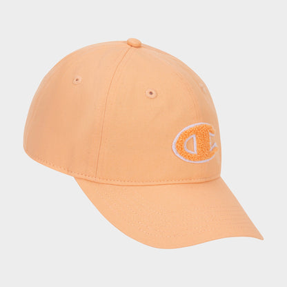 The Amber Chenille Adjustable Cap by Champion features a peach-colored, relaxed fit with a curved brim and an embroidered chenille “C” patch on the front left panel, displayed against a plain white background.