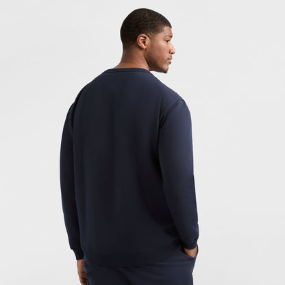A man faces away from the camera, wearing a dark navy Champion Powerblend Crewneck Sweatshirt, C Logo - Big & Tall and matching pants, set against a plain white background.