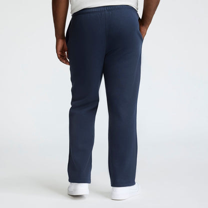 A person is seen from behind in Champion Powerblend Sweatpants, Open Hem, C Logo - Big & Tall, dark blue, paired with white sneakers, standing against a plain light background.
