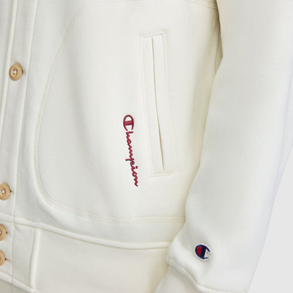 Close-up of a cream-colored Champion Fleece Baseball Jacket with a small embroidered logo on the sleeve and red cursive text near the pocket.