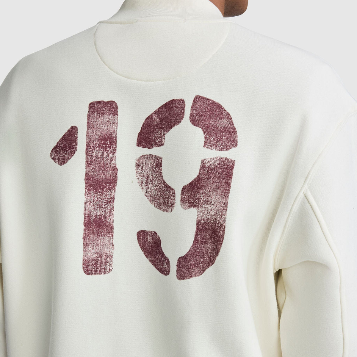 Back view of a white Champion Fleece Baseball Jacket with the number 19 in distressed, dark red print on the back.