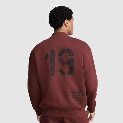 A person viewed from behind wearing a maroon Champion Fleece Baseball Jacket, featuring a large black 19 graphic and smaller printed text on the back.