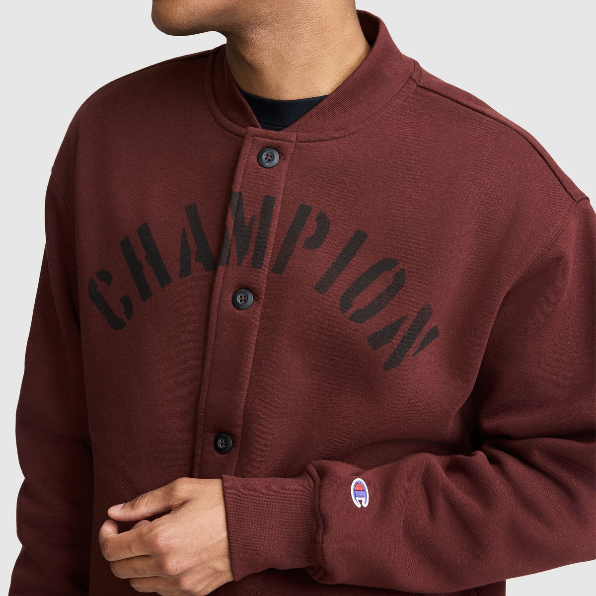 Maroon Champion Fleece Baseball Jacket featuring a black arched graphic on the chest and a small logo on the cuff.