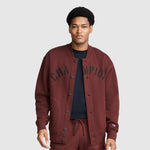 A person wearing a maroon Champion Fleece Baseball Jacket with black lettering across the chest.