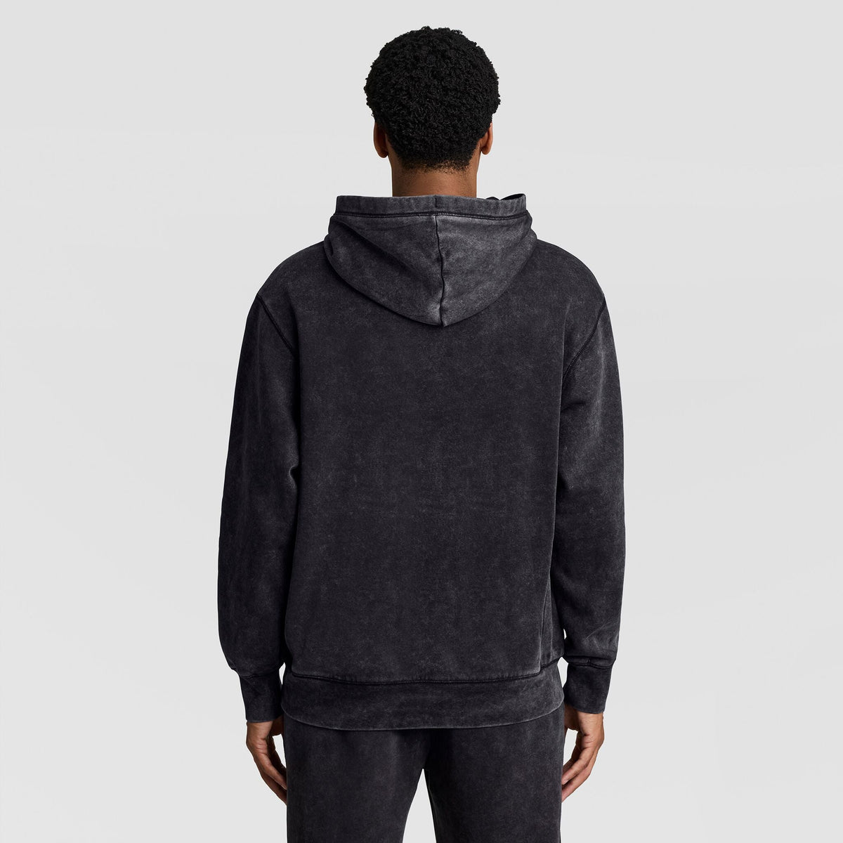 Back view of a person wearing a black Mineral Wash Pullover Hoodie, C Patch Logo with a drawstring hood.