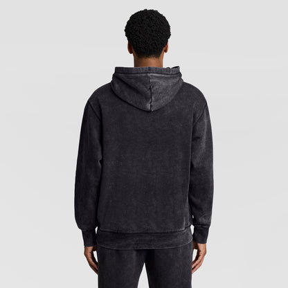 Back view of a person wearing a black Mineral Wash Pullover Hoodie, C Patch Logo with a drawstring hood.