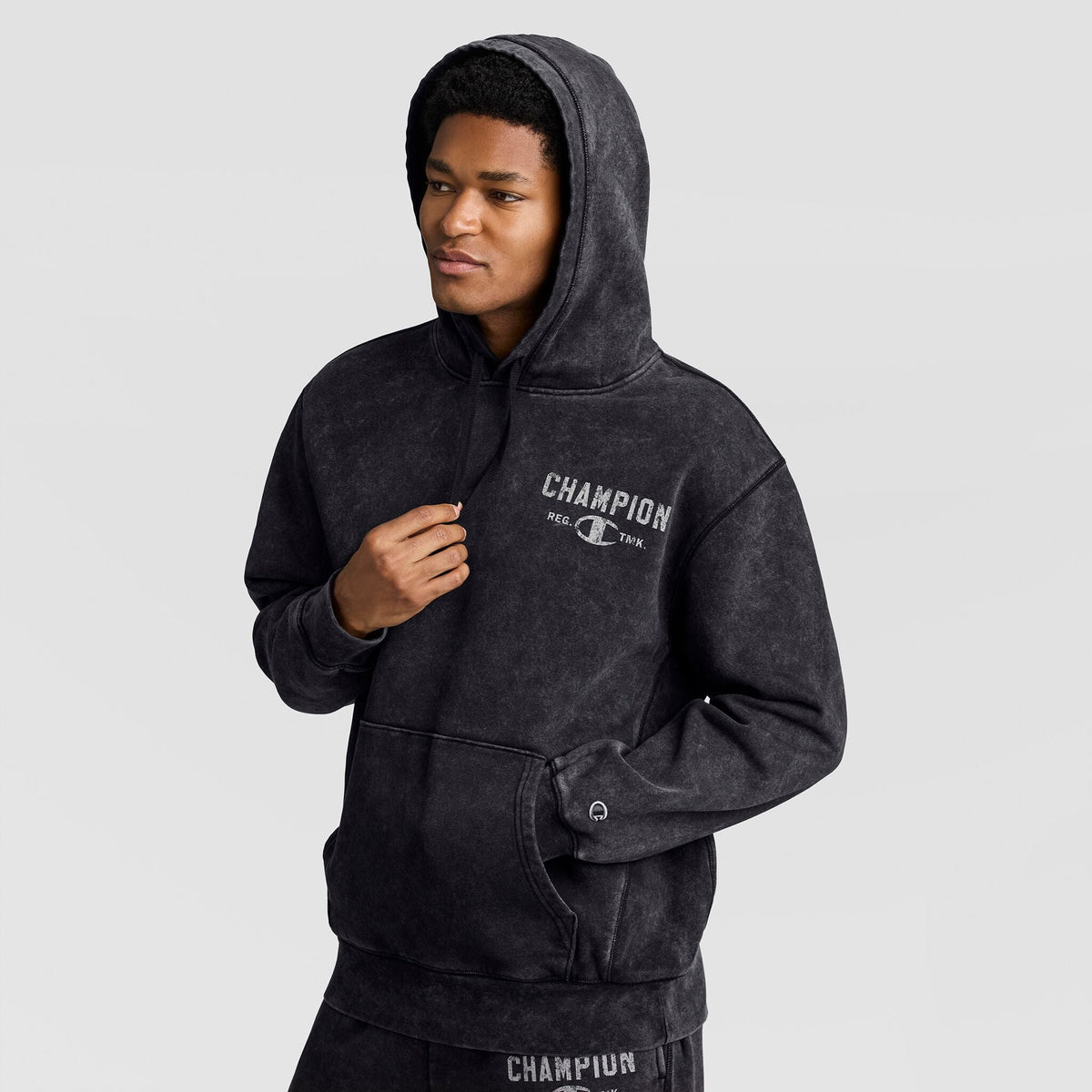 A man wearing a black Mineral Wash Pullover Hoodie, C Patch Logo with a chest logo and a small sleeve patch.