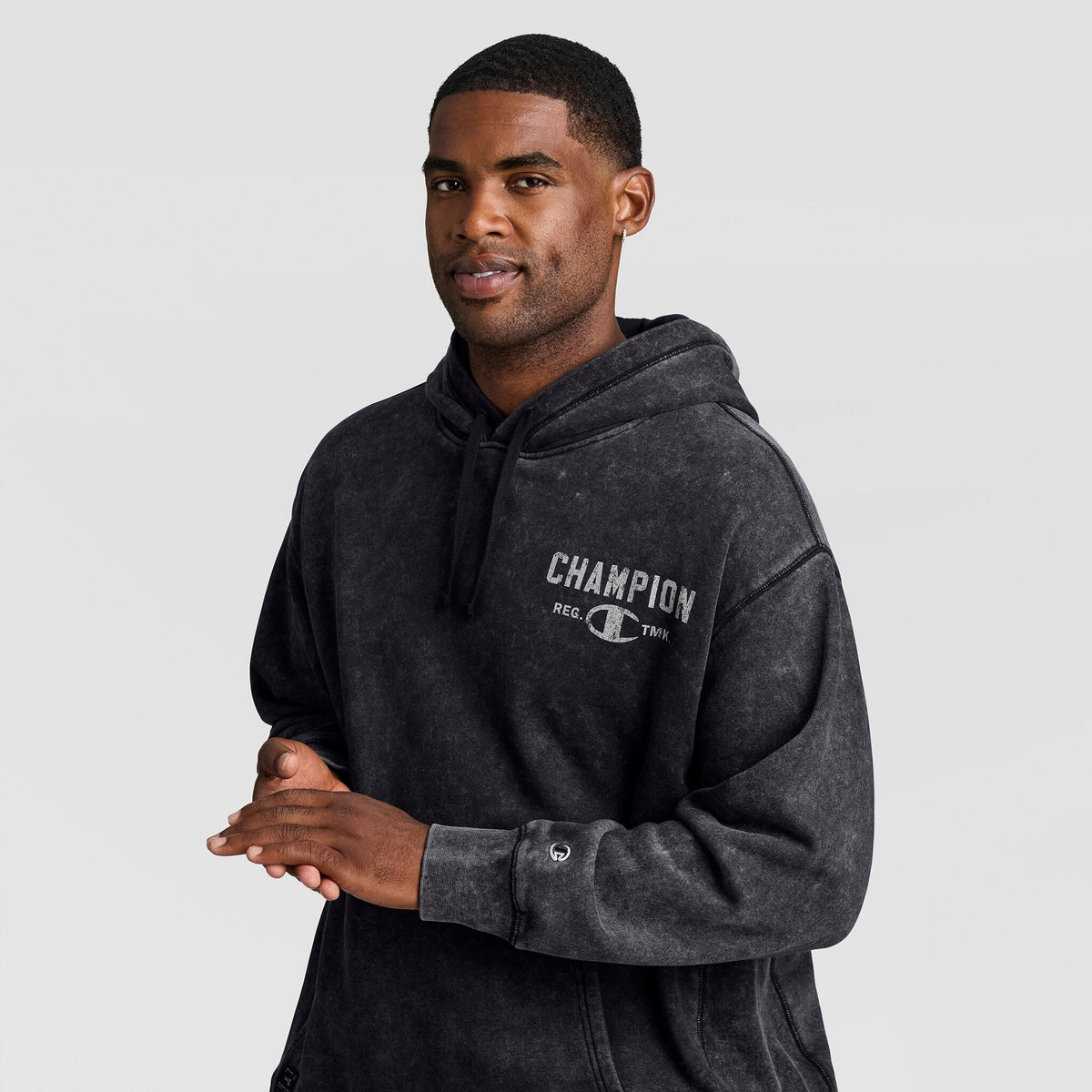 A man wearing a black Mineral Wash Pullover Hoodie, C Patch Logo featuring a chest graphic and a small patch on the cuff.