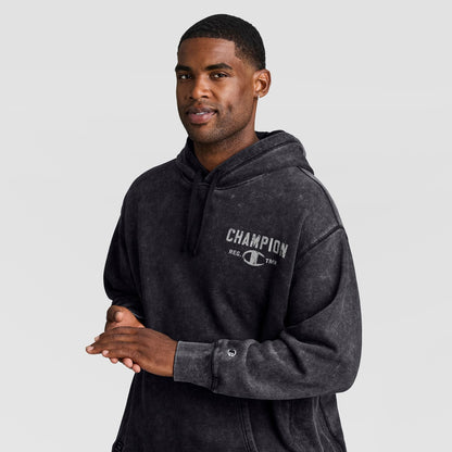A man wearing a black Mineral Wash Pullover Hoodie, C Patch Logo featuring a chest graphic and a small patch on the cuff.