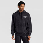 A man wears a black Mineral Wash Pullover Hoodie, C Patch Logo featuring a front kangaroo pocket and a distressed graphic logo on the chest.
