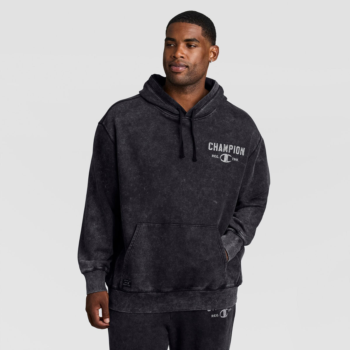 A man wearing a black Mineral Wash Pullover Hoodie, C Patch Logo, featuring a pouch pocket and a chest graphic.