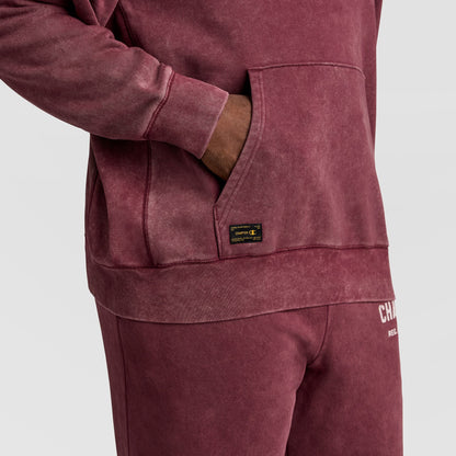 A maroon Mineral Wash Pullover Hoodie, C Patch Logo featuring a front kangaroo pocket and a small black rectangular brand patch, shown with matching sweatpants.