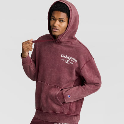 A man wearing a burgundy Mineral Wash Pullover Hoodie, C Patch Logo with a white logo on the chest and a small patch on the sleeve.