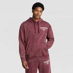 A man wearing a burgundy Mineral Wash Pullover Hoodie, C Patch Logo and matching sweatpants, both featuring printed logos.