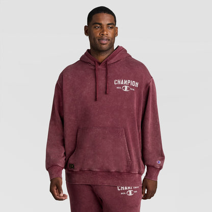 A man wearing a burgundy Mineral Wash Pullover Hoodie, C Patch Logo, featuring a graphic logo on the chest and a small patch on the sleeve.