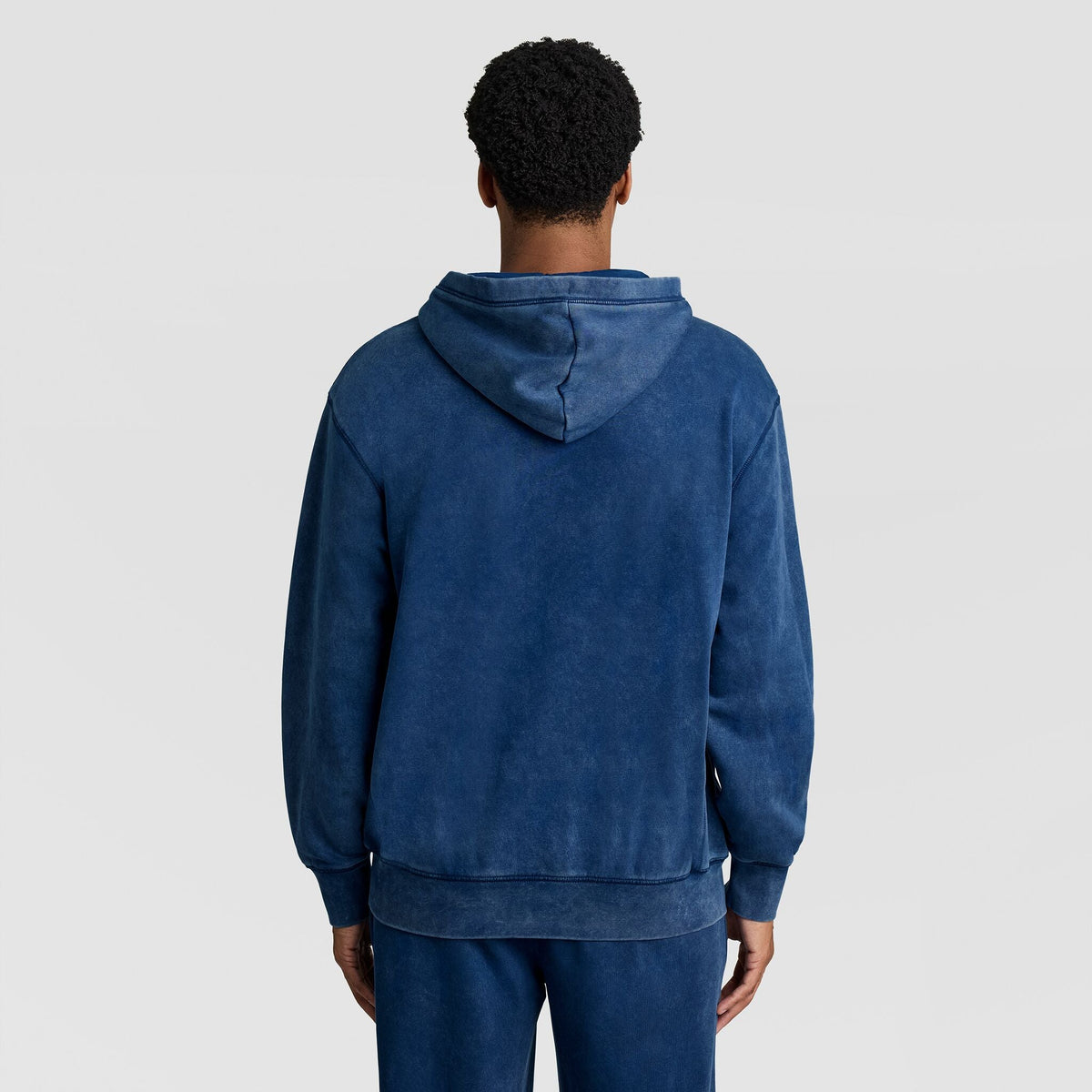 Back view of a person wearing a blue Mineral Wash Pullover Hoodie, C Patch Logo with the hood up.
